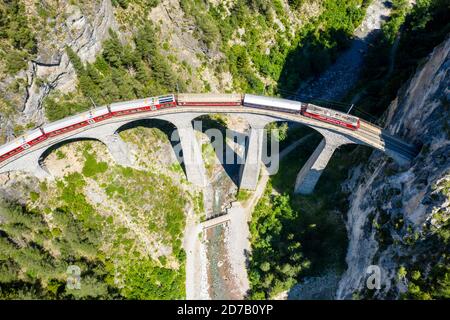 Atemberaubender Blick aus der Vogelperspektive auf den Zug vorbei am Landwasserviadukt in der Nähe von Filisur, roter Zug des Bernina Express, Schweiz Stockfoto