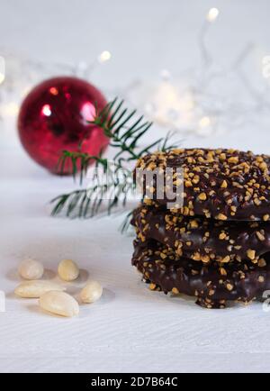 Advent- und Weihnachtsstimmung, Elisenlebkuchen mit Schokoladenvereisung und Haselnusskernen, auf einem weißen Holztisch im Hintergrund eine rote weihnachtskugel Stockfoto