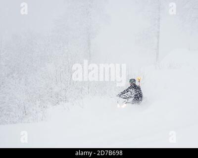 Ein Mann auf einem Schneemobil fährt durch Schneewehen in schwerer Schnee und Nebel Stockfoto