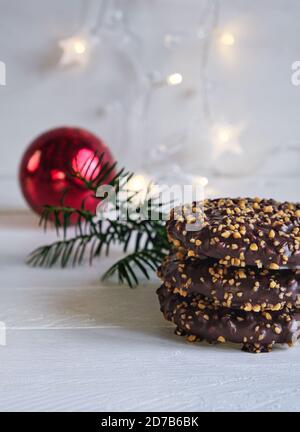 Advent- und Weihnachtsstimmung, Elisenlebkuchen mit Schokoladenvereisung und Haselnusskernen, auf einem weißen Holztisch im Hintergrund eine rote weihnachtskugel Stockfoto