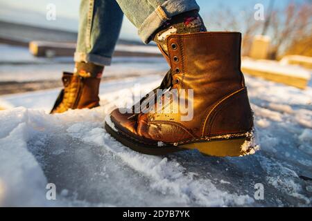 Der Winter kommt. Weibliche Stiefel auf rauer Slipper Eisfläche. Eine Frau in braunen Lederschuhen steigt die rutschige Eisleiter hinab. Stockfoto