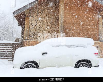 Ein schneebedecktes Auto ist in der Nähe einer Holzhütte auf geparkt Ein wolkiger Tag mit starkem Schnee Stockfoto