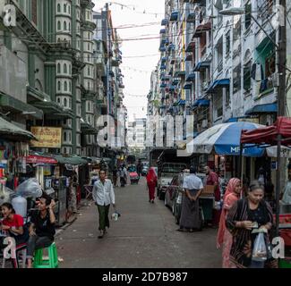 Yangon, Myanmar - 30. Dezember 2019: Der Alltag geschieht auf einer engen Straße in der Innenstadt mit geparkten Autos und Fußgängern zu Fuß Stockfoto