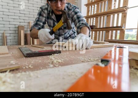 Tischler, der in der Werkstatt für Holzhandwerk arbeitet, um Baumaterial oder Holzmöbel herzustellen. Der junge asiatische Zimmermann verwendet professionelle Werkzeuge für Stockfoto
