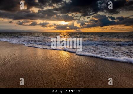 Die Sonne geht als Sonne am Meereshorizont unter Strahlen Platzen Durch Die Wolken Stockfoto