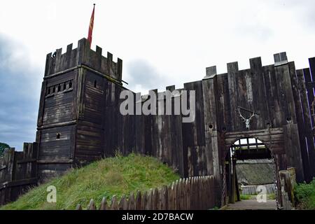 Hölzerne Burgmauern und ein Turm mit einer roten Flagge gegen einen bewölkten Himmel bei der authentischen Rekonstruktion des Stansted Mountfitchet Castle in Essex, England Stockfoto