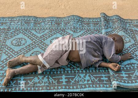 Ein kleiner Junge schläft auf einem Bürgersteig mit Teppich als Bettwäsche, Niamey, Niger Stockfoto