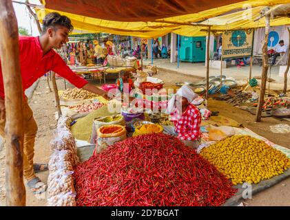 Kunden kaufen und bezahlen für Lebensmittel an einem Stand Verkauf Chilis, Gewürze und lokale Produkte in einem Straßenmarkt in einem Dorf in Madhya Pradesh, Indien Stockfoto