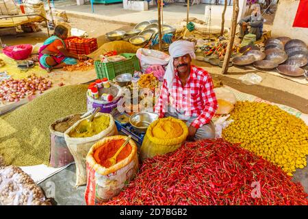 Lächelnder Stallholder sitzt an einem Stand, der rote Chilis, Gewürze und lokale Produkte in einem Straßenmarkt in einem Dorf in Madhya Pradesh, Indien verkauft Stockfoto