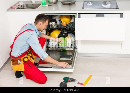 Männlicher Techniker, Der In Der Küche In Der Nähe Des Geschirrspülers Sitzt Stockfoto