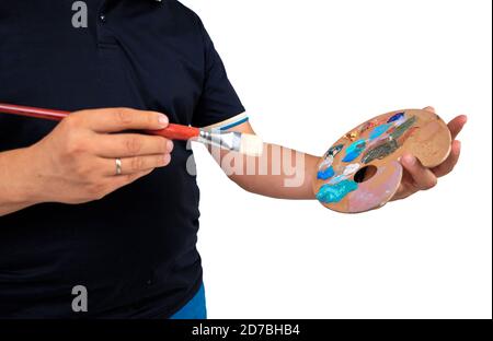 Bunte Farben und Pinsel liegen nebeneinander auf weißem Hintergrund. Das Kind hält einen Pinsel in der Hand Stockfoto