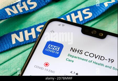 NHS COVID-19 App im Play Store auf dem Bildschirm des Smartphones neben viralen Masken und NHS Lanyard gesehen. Stockfoto