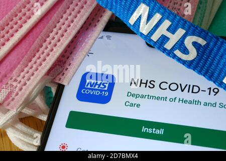 Manchester / Großbritannien - 17. Oktober 2020: NHS COVID-19 App im Play Store auf dem Bildschirm des Smartphones neben viralen Masken und NHS Lanyard zu sehen. Stockfoto