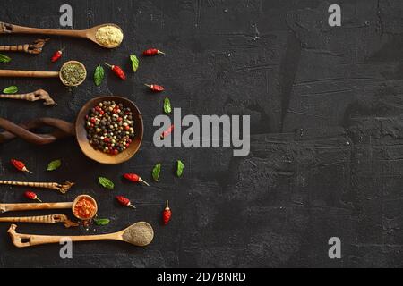 Verschiedene Arten von Gewürzen auf einem schwarzen Stein. Orientalische Gewürze in Löffeln, Paprika, Currypulver, Kräuter auf schwarzem Metallblech im asiatischen Stil. Flache Lay, Stockfoto