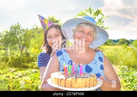 Großmutter Geburtstag, die mit einem Lächeln, zusammen mit ihrer Tochter im Dorf und hält einen Geburtstag hausgemachten Kuchen. Stockfoto