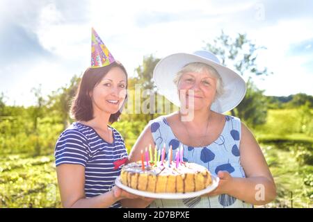 Großmutter Geburtstag, die mit einem Lächeln, zusammen mit ihrer Tochter im Dorf und hält einen Geburtstag hausgemachten Kuchen. Stockfoto