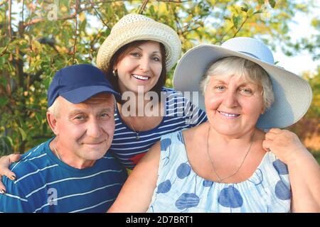 Schönes Seniorenpaar sitzt auf der Bank im Park mit ihrer erwachsenen Tochter. Oma und Opa umarmen und lächeln. Echte Liebe und Familie Stockfoto