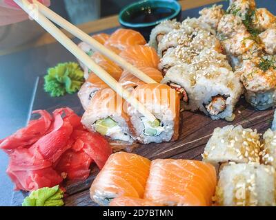 Mädchen Hand hält Essstäbchen und essen verschiedene Sushi-Rollen im Restaurant. Stockfoto