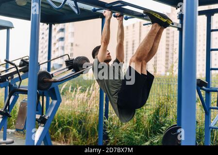 Aufnahme eines jungen Mannes, der Dips auf den unebenen Balken macht. Ein Mann zieht sich an einer horizontalen Stange hoch und hebt seine Beine an Gewicht. Sit-up. Stockfoto