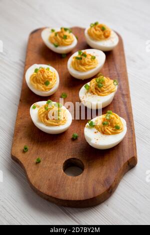 Hausgemachte deviled Eier mit Schnittlauch auf einem rustikalen Holzbrett auf einem weißen Holztisch, Seitenansicht. Stockfoto