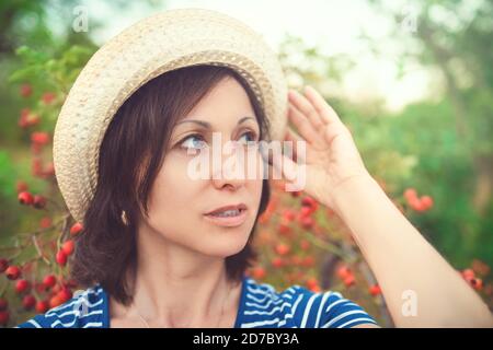 Bild der schönen Frau mittleren Alters tragen Strohhut lachend und Kamera beim Wandern im Sommer Park Stockfoto