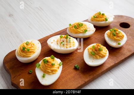 Hausgemachte deviled Eier mit Schnittlauch auf einem rustikalen Holzbrett auf einem weißen Holzhintergrund, niedrige Winkel-Ansicht. Stockfoto