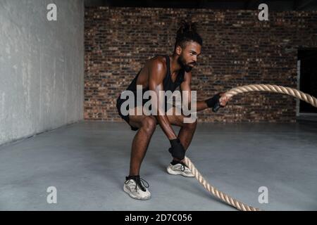 Bild des athletischen afroamerikanischen Sportlers, der mit Kampf ausarbeitet Seile im Innenbereich Stockfoto