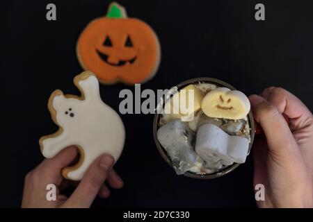 Draufsicht auf die´s Hände der Frau, die Becher mit gruseligen halloween halten Trinken und Geisterkeks Stockfoto