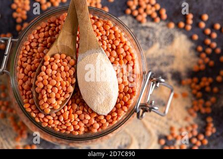 Rote Linsen und Linsenmehl in den Holzlöffeln über einer Schüssel rote Linsen. Stockfoto