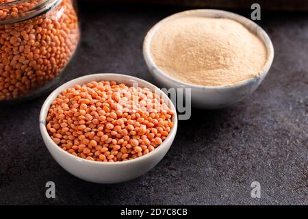 Rote Linsen und Linsenmehl in Schüssel auf dunklem Grund. Stockfoto