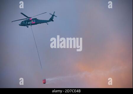 Aerial Brandbekämpfung Hubschrauber mit Feuereimer fliegen in Rauch zu Lassen Sie Wasser auf dem Lauffeuer fallen Stockfoto