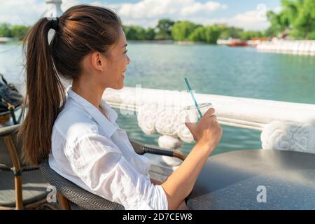 Glückliche junge asiatische Frau, die sich im Hafencafé am Wasser entspannen und trinken Kaltes Kaffee Getränk genießen Sommertag in der Stadt Am See Stockfoto