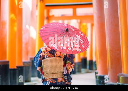 Geishas Mädchen mit japanischen kimono unter roten Holz- Tori Gate bei Fushimi Inari Schrein in Kyoto, Kimono ist ein traditionelles japanisches Gewand. Das Wort " Stockfoto