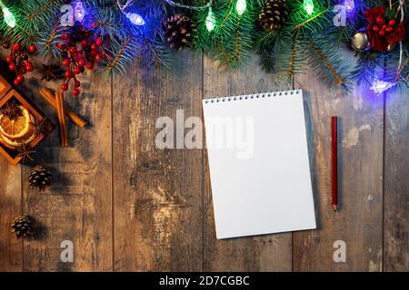 Erstellen einer To-Do-Liste oder eines Plans für das nächste Jahr. Christbaumzweig und Lichter auf Holzhintergrund. Schreiben eines Briefes an den Weihnachtsmann. Draufsicht mit Notizblock für Stockfoto