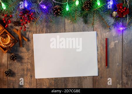 Neujahr oder Weihnachten Mockup. Vorlage für Brief an den Weihnachtsmann, Liste der Pläne und Ziele für Neujahr, Wunschliste in der Nähe FIR. Weihnachtsgirlande auf dunklem Holz Stockfoto