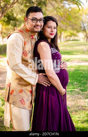 Junge asiatische indische schwangere Frau mit ihrem Mann tragen traditionelle Outfit steht im Park oder Garten Stockfoto