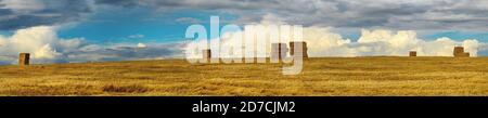 Ländliche sonnige Panoramalandschaft mit Heuhaufen in Farm Feld während Sonnenuntergang Stockfoto