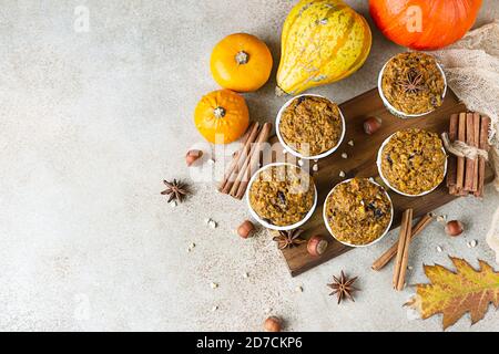 Holztablett mit veganen Kürbismuffins, Zimt und frischen Kürbissen auf hellem Betongrund. Herbst des Winters Backen. Draufsicht. Stockfoto