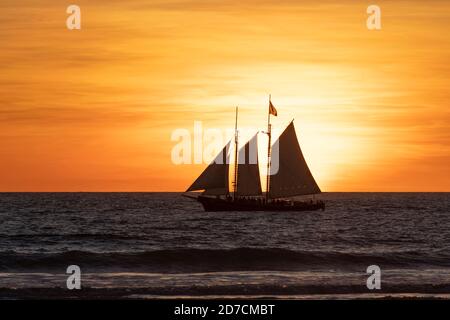 Ein Segelschiff, das Touristen auf eine Bootstour bei Sonnenuntergang vor dem Cable Beach von Broome bringt. Stockfoto