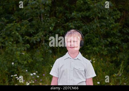 Ein lächelnder Junge mit Kopfhörern und spaziert im Park Im Sommer Stockfoto