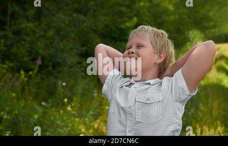 Ein lächelnder Junge im weißen Hemd steht im Sommer in einem Park. Hochformat Stockfoto