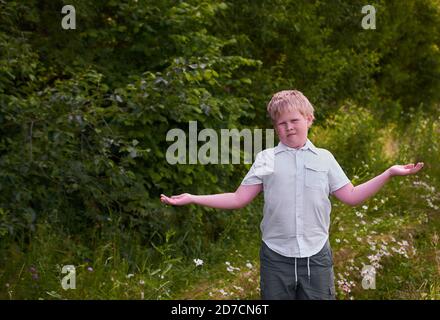 Ein verwirrter Junge wirft seine Hände auf einen Spaziergang Im Park im Sommer Stockfoto