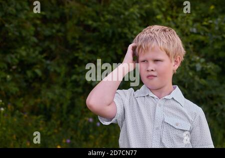 Ein verwirrter Junge kratzt sich beim Gang an seinem Kopf Der Park im Sommer Stockfoto