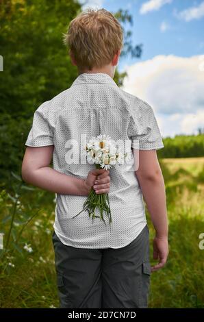 Ein Junge versteckt einen Haufen Gänseblümchen im Freien Luft hinter seinem Rücken Stockfoto