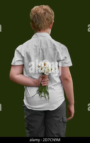 Der Junge versteckt einen Haufen Gänseblümchen hinter seinem Rücken. Rückansicht auf einem einheitlichen Hintergrund Stockfoto