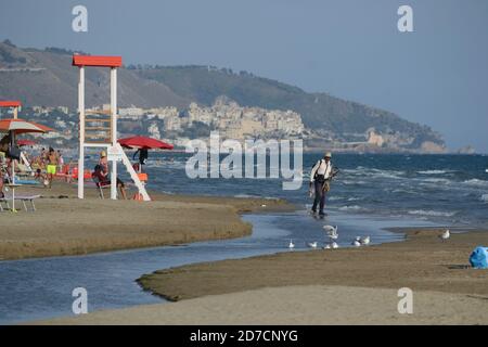 Ein freier Strand in der Nähe von Sperlonga im Sommer 2020. Ein nicht-EU-Bürger spaziert beladen mit Gegenständen, die er Badegäste zum Verkauf anbietet Stockfoto