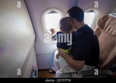 Vater und niedliche Kleinkind sitzen auf einem Flugzeug und Blick in den Himmel durch das Bullauge. First Flight Konzept, Reisen mit Kindern Stockfoto