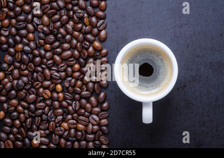 Gerösteter Kaffee Espressobohnen auf dunklem Hintergrund und Tasse mit Crema, close-up, flat lay, Hintergrund, Stillleben, heißes Getränk, Ich liebe Kaffee-Konzept Stockfoto