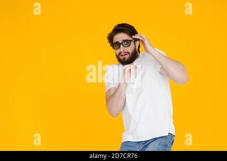 Porträt eines zotteligen, bärtigen, verängstigten Mannes in 3D-Brille mit offenem Mund und großen Augen, auf gelbem Hintergrund. Stockfoto