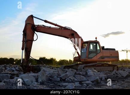 Raupenbagger mit Hydraulikhammer bei Sonnenuntergang. Zerstörung, Abriss von Beton und Hartgestein auf der Baustelle oder im Steinbruch. Jackh Stockfoto